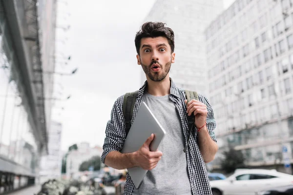 Sırt çantalı ve dizüstü bilgisayarlı heyecanlı bir turist sokakta yürüyor.