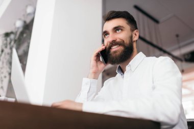 Modern ofiste oturan başarılı yakışıklı iş adamı, dizüstü bilgisayar ve akıllı telefonu yeni başlattığı proje için kullanıyor. Sivri sakallı adam telefonda ortağıyla iş anlaşmalarından bahsediyor.