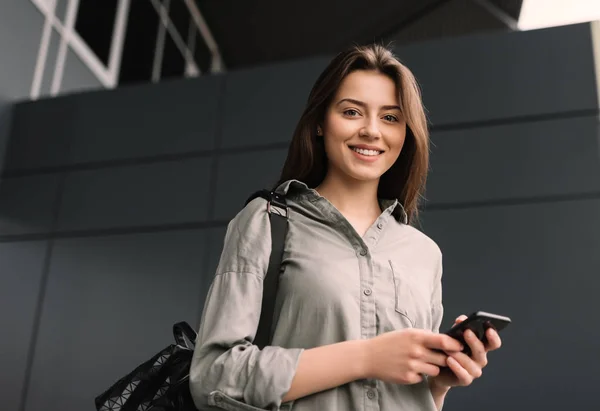 Portrét Pozitivního Usměvavého Vysokoškolského Studenta Používajícího Mobilní Telefon Pro Vyhledávání — Stock fotografie