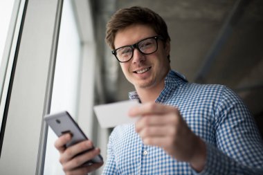 Yakışıklı adam kartvizit ve cep telefonu loft ofisinde tutuyor. İyi giyimli işadamı bilgi online araştırma şık gözlüklü. Adam çağrı kapalı bir taksi gülümseyen.