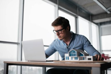 Dizüstü bilgisayar kullanan, araştırma, ev modeli ile çalışma, ofiste yaratıcı çözüm arayan proje planlama başarılı mimar. Brainstorming.Portrait Tasarımcısı işyerinde. 