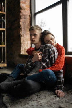 Çatı katı modern daireler içinde genç güzel aile portresi. Sevimli kadın kocasını rahat evde sarılma. Güzel çift pencere yakınındaki halı üzerinde oturan birlikte. 