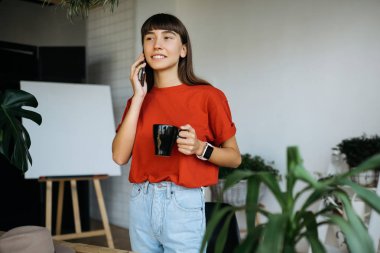 Neşeli gülümseyen serbest meslek yılında modern ofis telefon konuşma. Rahat iç ayakta başarılı ve şık çiçek dükkanı sahibi portresi. Smartphone ve kahve tutan hipster kadın. 