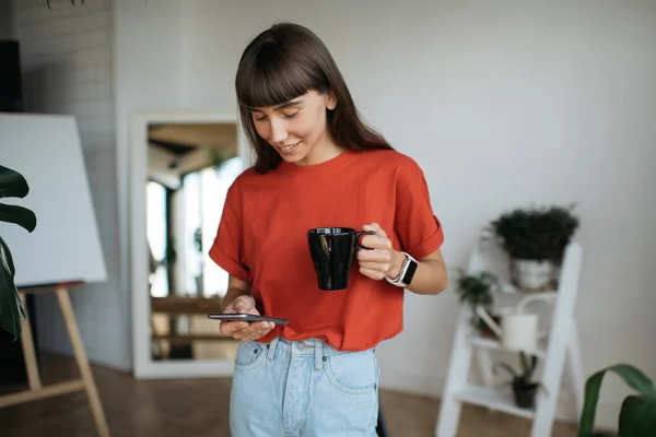 Sohbet, smartphone, kullanarak kırmızı tişörtlü onay posta kutusu, başarılı ve şık kadın portresi bilgi araştırma. Kahve modern ofis çalışma proje tutan hipster kadın. Freelancer iş başında. 
