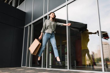 Başarılı mutlu kadın müşteri ile kablosuz kulaklık kullanarak ve Alışveriş Merkezi yakınındaki alışveriş torbaları ile sokakta çalışan güzel gülümseme müzik dinleme. Siyah Cuma kavramı. Satış iskontosu. 