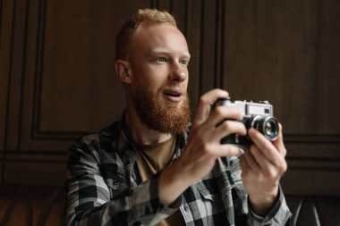 Profesyonel fotoğrafçı portresi kapatın. Genç hipster adam gezgin olumlu duygusal yüz tutan retro kamera ve alma resim sakallı. Paparazzi veya özel dedektif iş başında. 