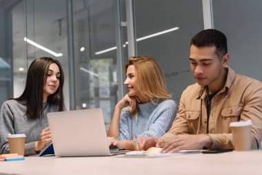 Group of multiracial university students using laptop computer working project together sitting at table, talking, learning language, exam preparation. Teamwork. Colleagues brainstorming. Meeting 