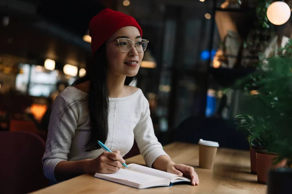 年轻有吸引力的大学生学习 考试准备 愉快的亚洲女人穿着时尚的红帽子和眼镜写笔记 规划工作过程 坐在阁楼咖啡馆 韩国嬉皮士自由职业者在工作场所的肖像 — 图库照片