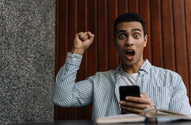 Mutlu duygusal yüzü, ağzı ve gözleri açık Afrikalı Amerikalı adam online poker piyangosunu kazandı. İnternetten alışveriş için mobil uygulama kullanan bir adam. İndirimli satışlar, nakit ödeme, düşük fiyatlar. Kara Cuma konsepti