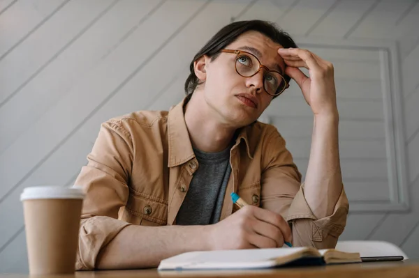 Busy, tired man have no idea what to do, he looking for creative solution, thinking, brainstorming at workplace. Portrait of pensive hipster guy in stylish eyeglasses working freelance project