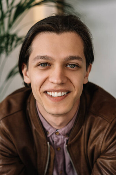 Authentic portrait of successful young man with happy emotional face and white teeth posing for pictures. Positive hipster wearing casual clothes laughing, sitting in cafe. Blurred background 