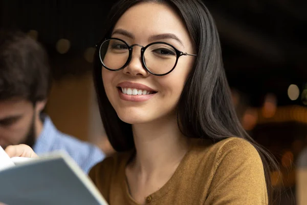 スタイリッシュなメガネで笑顔のアジアのビジネスウーマンの肖像画をクローズアップ写真 図書館で勉強するポジティブな学生 言語を学ぶ 試験の準備 手にノートを持つ 教育の概念 — ストック写真