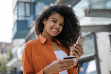 Kredi kartı tutan Afro-Amerikalı kadın, düşük fiyatlarla ve nakit geri online alışveriş için mobil uygulama ile akıllı telefon kullanarak. Mutlu hipster kız gıda online sipariş, işlem yapma 