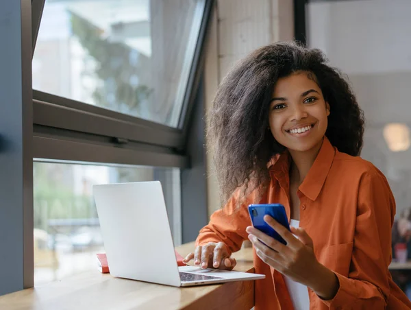 Ofiste çalışan genç bir kadın. Dizüstü bilgisayar ve internet kullanarak, cep telefonu tutan Afrikalı Amerikalı iş kadını Portresi. Başarılı iş ve kariyer konsepti 
