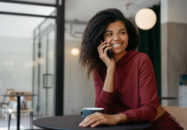 Genç, güzel, Afro-Amerikan bir kadın cep telefonuyla konuşuyor, gülüyor, iletişim kuruyor. Neşeli kıvırcık saçlı hippi kız cep telefonu kullanıyor, modern kafede kahve içiyor. 