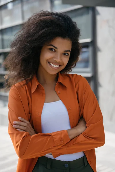 Attractive African American businesswoman with arms crossed standing outdoors and laughing. Successful business and career concept. Portrait of young woman leader, entrepreneurship, start up