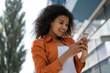 Genç heyecanlı Afrikalı Amerikalı kadın internetten yemek sipariş ediyor. Güzel kıvırcık saçlı hippi kız internet üzerinden alışveriş yapmak için akıllı telefon uygulaması kullanıyor. Düşük fiyatlar, satışlar. Kara Cuma konsepti