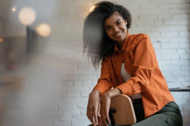 Güzel gülümseyen yüzlü, kıvırcık saçlı, çatı katındaki kafede oturan genç ve çekici Afro-Amerikan kadın portresi. Pozitif karışık ırk modelleri resimler için poz veriyor, gülüyor. 