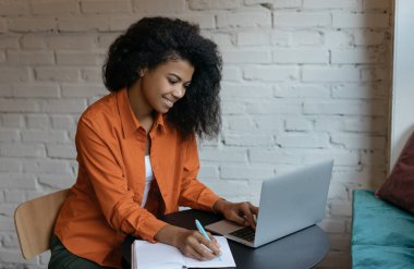 Başarılı bir üniversite öğrencisi, Laptop bilgisayar ve internet kullanarak dil öğreniyor. Genç mutlu Afrikalı Amerikalı kadın internet sitesinden iş eğitimi kurslarını izliyor, not alıyor. 