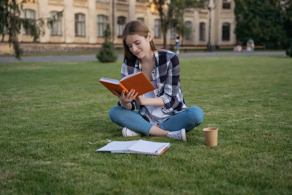 Student studying, reading a book, learning language, exam preparation, sitting on grass. Portrait of young happy woman with emotional face working in park. Education concept