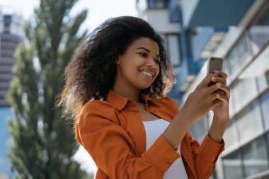 Neşeli Afrikalı Amerikalı kadın elinde cep telefonu, iletişim, sohbet, internet sitesinde bilet rezervasyonu. Gülümseyen hippi kız internetten yemek sipariş etmek için mobil uygulamalı akıllı telefon kullanıyor. Mobil bankacılık