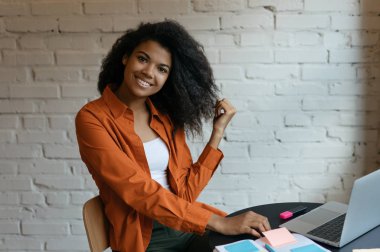 Kendine güvenen genç bir iş kadınının portresi dizüstü bilgisayar kullanıyor, başlangıç projesinde çalışıyor, strateji planlaması yapıyor, modern ofiste oturuyor. Başarılı Afrikalı Amerikalı öğrenci eğitim, öğrenim dili, çevrimiçi eğitim