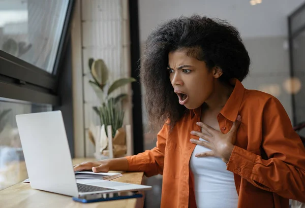 Portrait of stressed freelancer looking at laptop screen, missed deadline, fired from job. Emotional African American woman watching breaking news