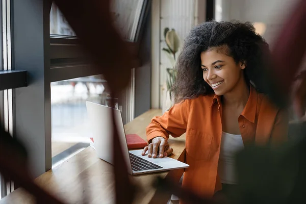 Beautiful African American woman watching online training courses for successful business in office. Portrait of happy designer using laptop computer and internet, working freelance project remotely
