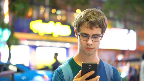 Young Man Taking a Call and Texting at Night On Smartphone With Busy Urban Background - Model Released