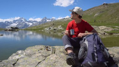 Mutlu genç Hiker pişirme çay / kahve üzerinde kamp sobası