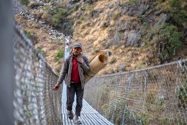 Gorkha, Nepal - 18 Aralık 2018: Nepal uzak köy içinde peşinden koyun sürüsü ile bir asma köprü üzerinde yürüyen bir genç çoban.