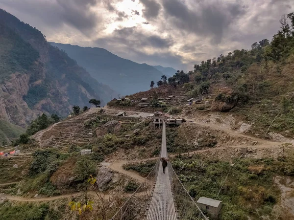 Porter crossing suspension bridge in remote village of Nepal