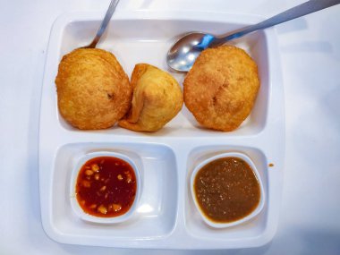 Samosa ve kachori chutney veya sos ile beyaz bir tabakta servis edilir. Üstte görüntü