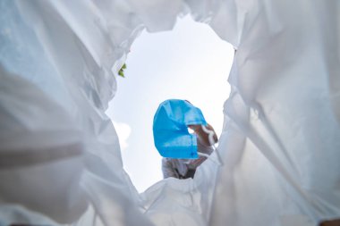 Tek kullanımlık cerrahi maskeyi çöpe atan bir adamın düşük açılı görüntüsü. Beyaz arkaplanda hijyenik maske.