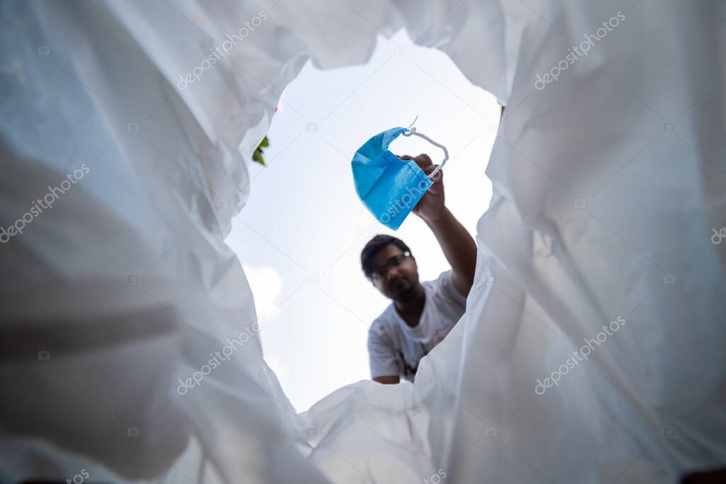 Low angle view of a man throwing disposable surgical mask into the bin. Hygienic mask on white background.