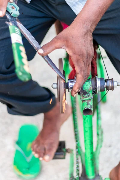 Closeup hands of a man sharpening a knife on a DIY makeshift sharpening machine on a bicycle frame.