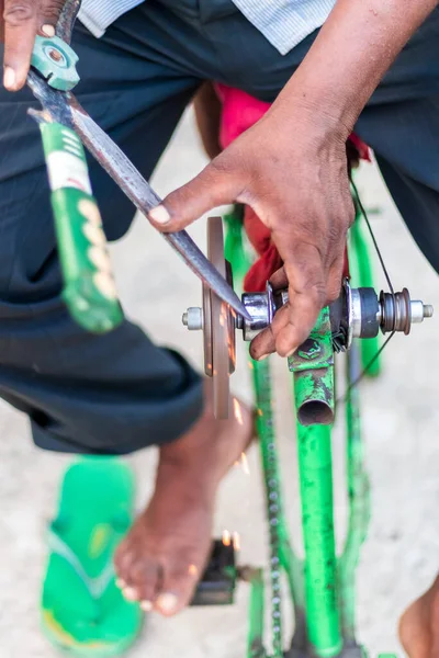 Closeup hands of a man sharpening a knife on a DIY makeshift sharpening machine on a bicycle frame.