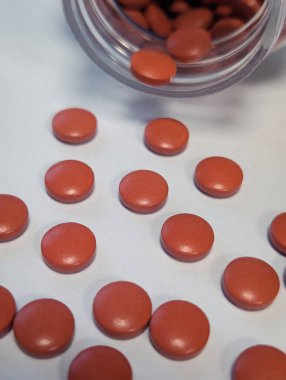 Yuvarlak tabletlerin dikey fotoğrafı beyaz arka planda ilaç şişesiyle dağılmış.