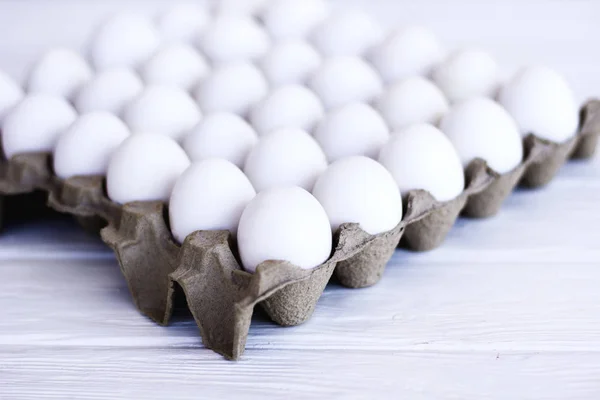 White eggs in a package on a white wooden background