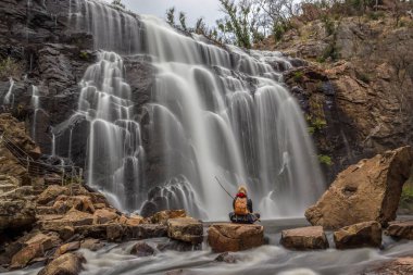 bir kayaya Mackenzie Falls önünde oturan kadın