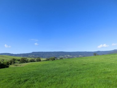 Küçük tepelerde yeşil çim alan ve bulutlar ile mavi gökyüzü, Avustralya