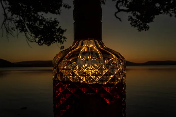 Bella bottiglia di rum pieno di rum che tiene davanti a un tramonto sul lago Watson Taylors a Crowdy Bay National Park, Nuovo Galles del Sud, Australia — Foto Stock