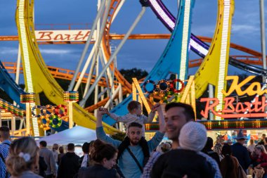 Munich, Germany - 2019 September 24: a father is carrying his young son on his shoulders in front of a 5 loop roller coaster on the oktoberfest