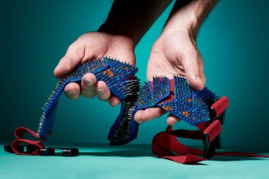 Erkeklerin elleri, okyanus arka planında metal iğneli, dikenli, mavi-kırmızı bir masaj kemerini tutuyor. Yan görünüş. Sağlıklı bir yaşam tarzı. Rahatlama ve sağlık için..