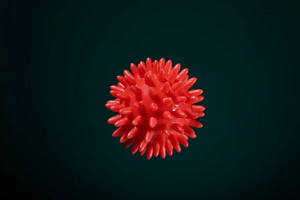 Beautiful red massage ball with spikes for stimulation and circulation, hangs in the air on the dark green background. relaxation, health. Thematic and subject-matter shooting. bacterium.