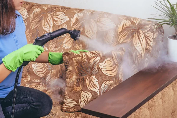 掃除だ 緑の手袋の少女は 蒸気発生器でソファと家具をきれいにします 微生物を殺す アパートの清掃サービス ブルーTシャツ — ストック写真