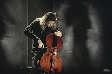Kyiv, Ukraine, 05.11.2019: Apocalyptica performance. The melodic game of Eicca Toppinen on cello with steep staged light. Shooting in the dark. Magic concert atmosphere clipart
