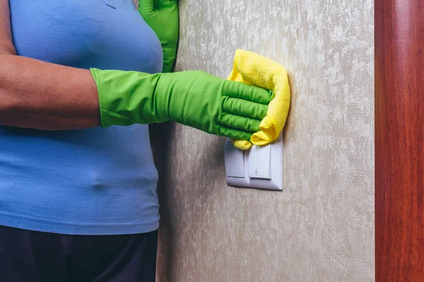 Cleaning in the house. A girl in green gloves wipes the electricity switch with a yellow cloth. cleaning from dust. Cleaning of a surface. experienced worker. close up.