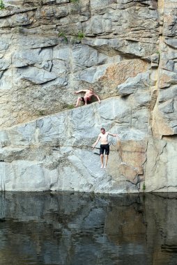Korostyshev, Ukrayna, 08.06.2020, adam kayalara tırmanıyor. İkinci adam bir uçurumdan suya atlar, yüksekten. Çatlaklarla kaplı bir yüzey. Taş gibi. Taş duvarlar. Korkusuz insanlar.