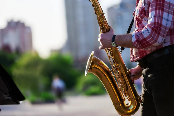 Saxofonist spielt ein goldenes Saxophon auf der Straße, in Sichtweite von Passanten. Frühling. Bläserklänge. Zunge Holzblasinstrument. Bokeh. — Stockfoto